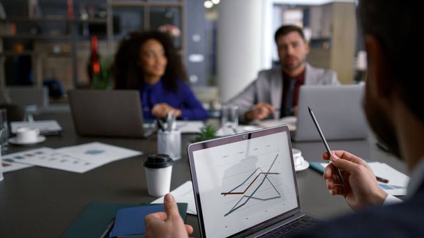 Πολυεθνικοί επιχειρηματίες συζητούν γραφήματα γραφημάτων χρησιμοποιώντας υπολογιστή σε συνεδριακή συνάντηση - Φωτογραφία, εικόνα