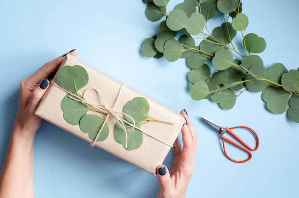 Caja de regalo envuelta en papel marrón decorado con rama de eucalipto, idea de envoltura de regalo de cero residuos ecológico natural. Vista superior. - Foto, imagen