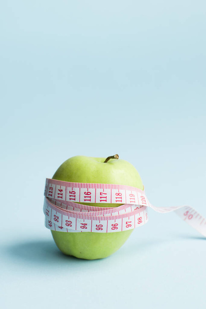 Manzana con cinta métrica sobre fondo azul. Pérdida de peso, conteo de calorías y concepto de alimentación saludable: calcule la ingesta diaria de nutrición. Copiar espacio. - Foto, imagen