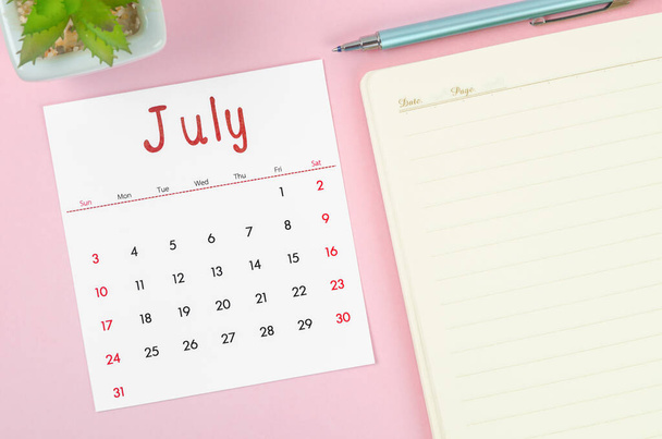 Kalendarz z lipca 2022 r. z notatnikiem na różowym tle. - Zdjęcie, obraz