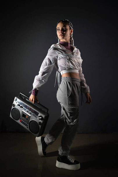 Young woman holding a retro tape recorder with one hand and looking away in studio shot - Photo, Image