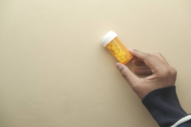 mladý muž ruka drží oranžové barvy pilulky kontejner  - Fotografie, Obrázek