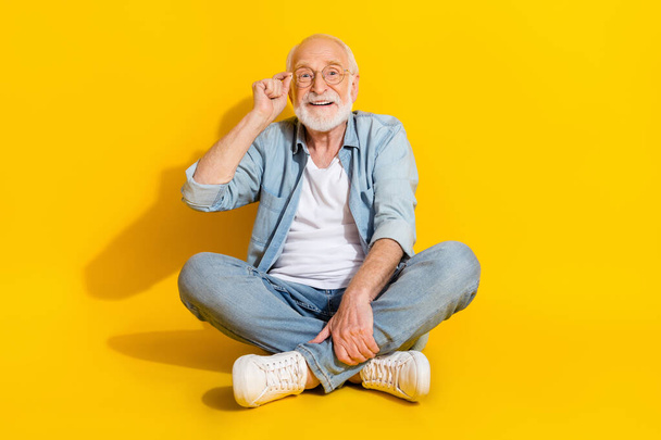 Portrait of attractive confident smart clever cheerful grey-haired man sitting touching specs isolated over bright yellow color background. - Fotoğraf, Görsel