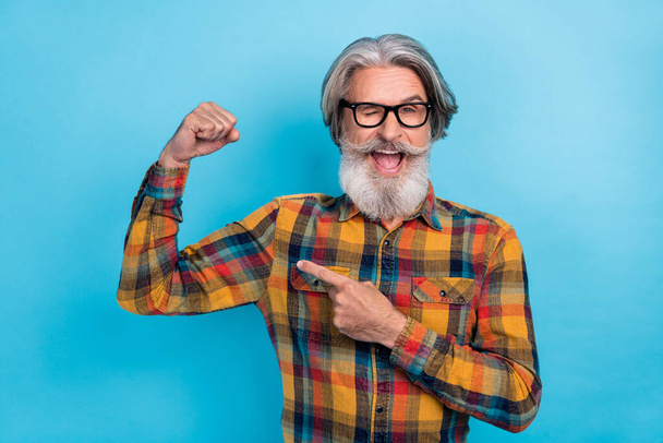 Photo of mature man point finger arm muscles ad recommend promo sporty blink eye isolated over blue color background. - 写真・画像