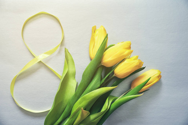 Five yellow tulips on a grey background with the number eight made of ribbon - Fotó, kép