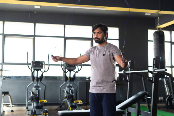 young indian body builder warming up body by skipping rope before starting workout at gym - concept of fat loss, bodycare and wellness. - Zdjęcie, obraz