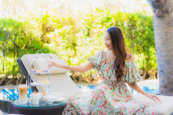 Mooi portret jonge aziatische vrouw met namiddag thee set met koffie zitten op stoel rond zwembad in hotel resort - Foto, afbeelding