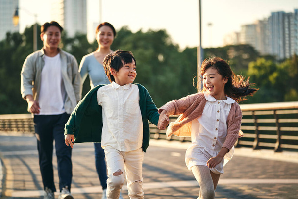 シティパークの歩道橋を歩いている2人の子供を持つ幸せなアジアの家族 - 写真・画像