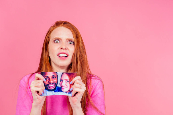 redhaired ginger sad woman tearing photo of happy international couple - Fotó, kép