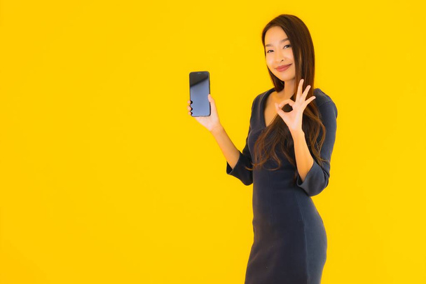 Portré gyönyörű fiatal ázsiai nő okos mobiltelefon vagy mobiltelefon sárga elszigetelt háttér - Fotó, kép