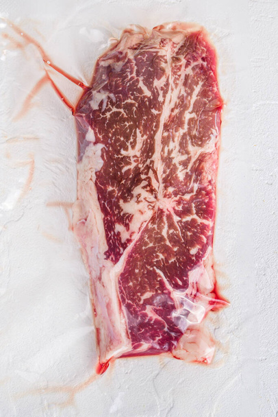 Top blade hovězí steak, vakuově balené organické maso pro sous vide vaření na bílém betonu texturované pozadí, horní pohled - Fotografie, Obrázek