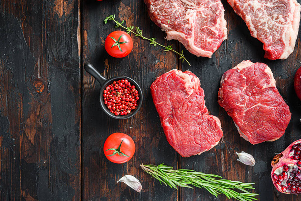 Nyers bio marhahús steakek farok, fűszerekkel és fűszernövényekkel a régi rusztikus sötét fa háttér, felső nézet helyet a szöveges - Fotó, kép