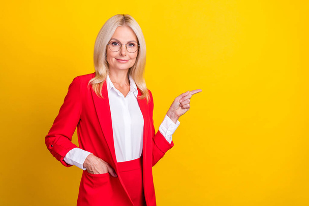 Photo of pretty aged business woman indicate finger empty space choice select ads isolated over yellow color background. - Fotografie, Obrázek
