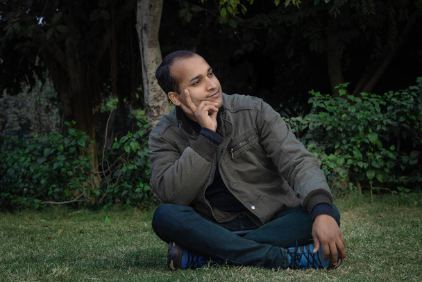 junger Mann verschiedene Stimmungen des Ausdrucks Kreuz Bein sitzt in einem Park aus flachem Winkel - Foto, Bild