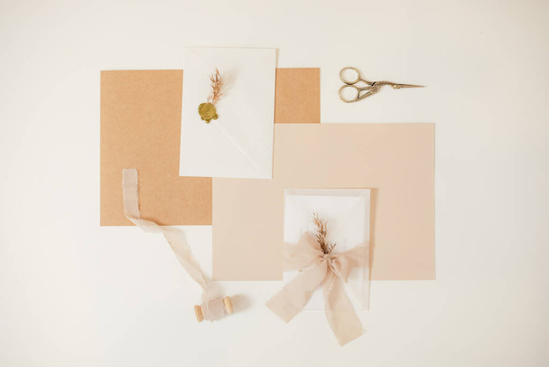 Peach mock up composition of paper weeding envelopes with ribbons, herb. scissors, cut out handmade jobbing. Top view.  - Фото, зображення