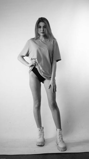 Schwarz-Weiß-Foto einer jungen schönen Frau mit langen Haaren im T-Shirt im Studio.   - Foto, Bild