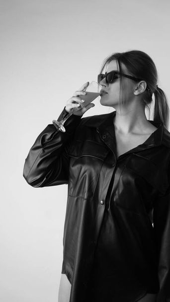 Black and white photo of young beautiful woman wearing in black shirt and sunglasses posing in studio.   - Valokuva, kuva