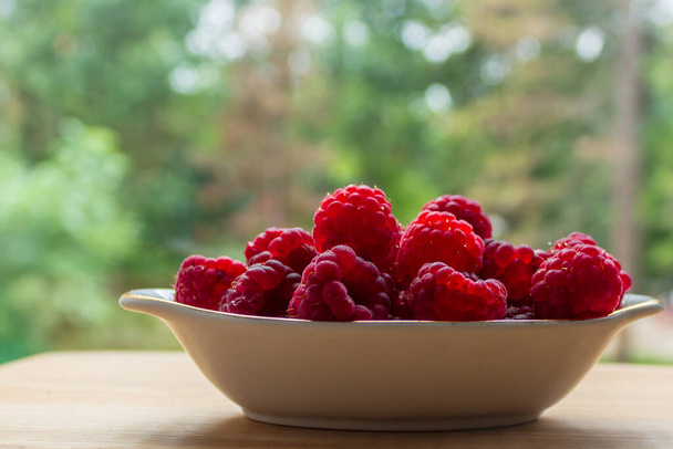 Raspberry berries in a vase on the table. Close-up on a blurred background. - Photo, Image