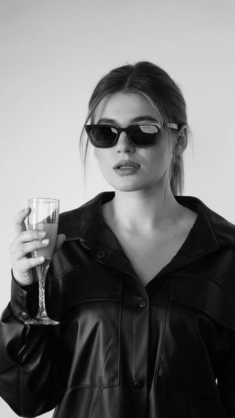 Black and white photo of young beautiful woman wearing in black shirt and sunglasses posing in studio.   - Foto, immagini
