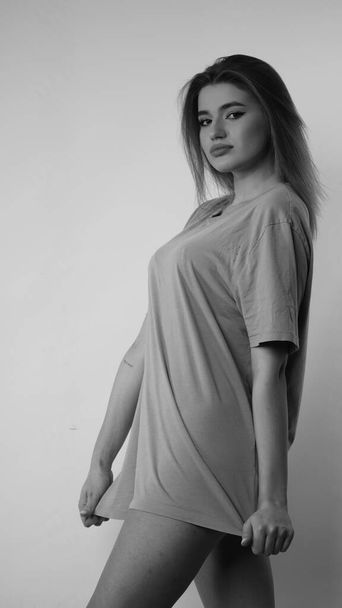 Black and white photo of young beautiful woman with long hair wearing in t-shirt in studio.   - Fotografie, Obrázek