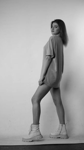 Zwart-wit foto van jonge mooie vrouw met lang haar in t-shirt in studio.   - Foto, afbeelding