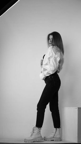 Schwarz-Weiß-Foto einer jungen schönen Frau mit langen Haaren im Hemd, die im Studio posiert.   - Foto, Bild