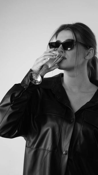 Foto en blanco y negro de una joven hermosa vestida con camisa negra y gafas de sol posando en el estudio.   - Foto, Imagen