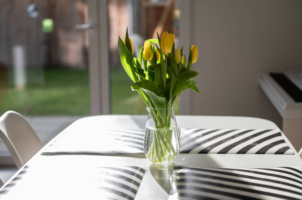 Beautiful glass vase with sresh yellow flowers on table in spring sunlights - Φωτογραφία, εικόνα