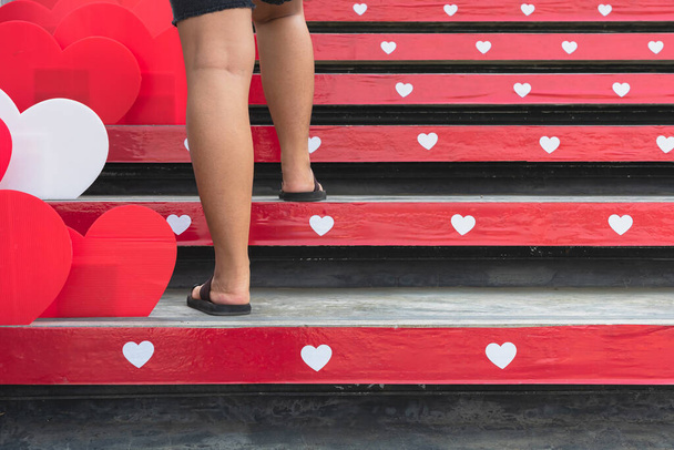 Pies de mujer joven subiendo escaleras con hermosa forma de corazón rojo y blanco hecho de láminas de plástico corrugado decoración en las escaleras con motivo del festival del amor de San Valentín. Enfoque selectivo - Foto, imagen