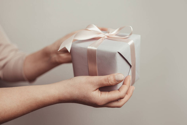 Nahaufnahme von Frauenhänden mit Überraschungsgeschenkverpackung auf rosa Pastellhintergrund mit Kopierraum. Weihnachten, Neujahr, Valentinstag und Geburtstagskonzept - Foto, Bild