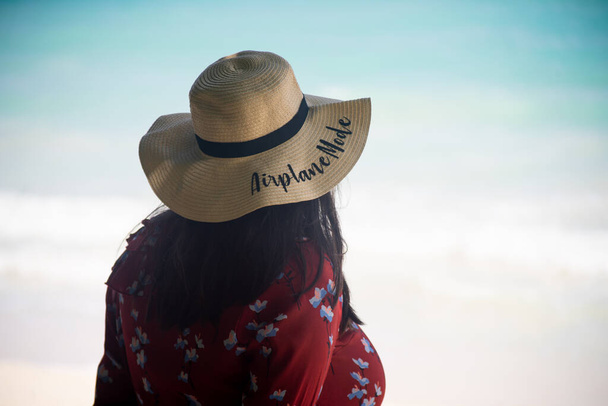 young woman a straw sun hat with aeroplane mode standing on beach with blue green waves lapping the shore in the andaman islands at swaraj dweep havelock a tropical vacation spot - 写真・画像