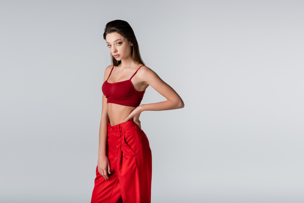 young model in red outfit posing with hand on hip isolated on grey - Foto, Imagem