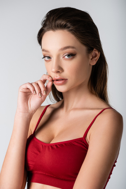 young pretty woman in red crop top looking at camera isolated on grey - Photo, Image