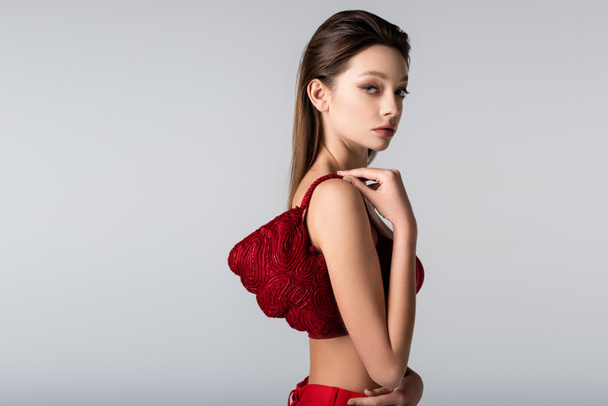 young woman carrying red stylish bag on shoulder isolated on grey - Fotografie, Obrázek