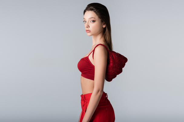pretty woman in red outfit with stylish bag on shoulder isolated on grey - Фото, зображення
