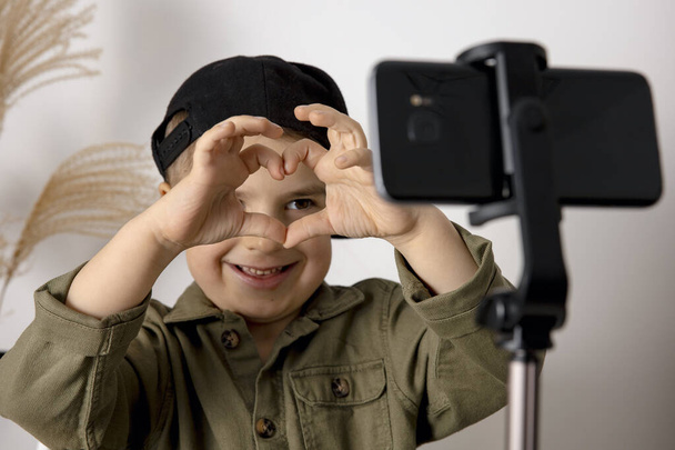 Αξιολάτρευτο, χαριτωμένο, μικρό αγόρι blogger καταγραφή lifestyle blog, μιλώντας στην κάμερα του smartphone στο τρίποδο. Ο νεαρός επιρροή τραβάει βίντεο για το κανάλι του. Παιδί κάνει βίντεο για τους οπαδούς του σε απευθείας σύνδεση. - Φωτογραφία, εικόνα