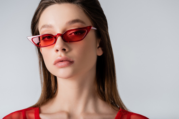 young model in red trendy sunglasses looking at camera isolated on grey - Фото, зображення