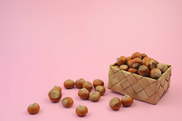 Hazelnuts in a decorative basket on a pink background. Nuts - healthy food. Harvesting nuts - Φωτογραφία, εικόνα