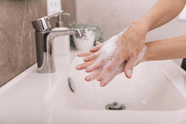 Washing hands under the flowing water tap. Hygiene concept hand detail. Washing hands rubbing with soap for corona virus prevention, hygiene to stop spreading corona virus in or public wash room - Foto, imagen