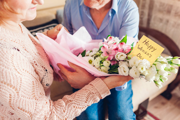 幸せな女性の日、 8 3月の贈り物。女性は自宅で春の黄色の花を咲かせるグリーティングカードを保持しています - 写真・画像