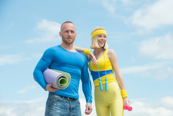 Fitness man and woman in training. Young happy couple in headbands with dumbbells and fitness mat outdoor. - 写真・画像