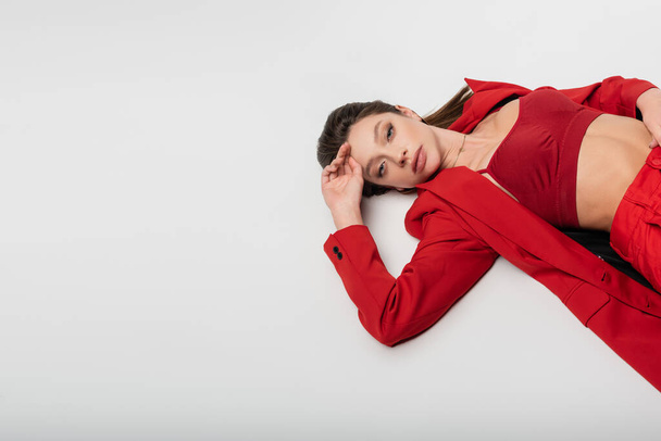 high angle view of trendy young woman in red suit lying isolated on grey - Photo, image