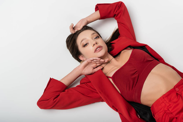 top view of trendy young woman in red suit lying on grey - Foto, afbeelding