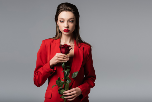 young woman in red blazer holding rose isolated on grey - 写真・画像