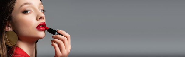 close up de jovem aplicando batom vermelho isolado em cinza, banner - Foto, Imagem