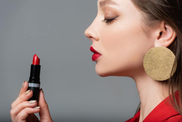 side view of young model holding red lipstick isolated on grey - 写真・画像
