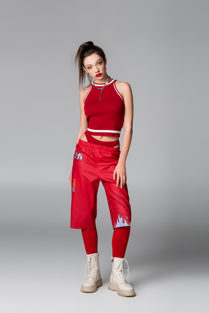 full length of young woman in red sportive outfit posing on grey - Foto, Imagem