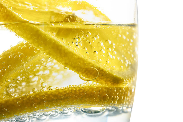 Свіжий шматочок лимона у воді з бульбашками у склянці
. - Фото, зображення