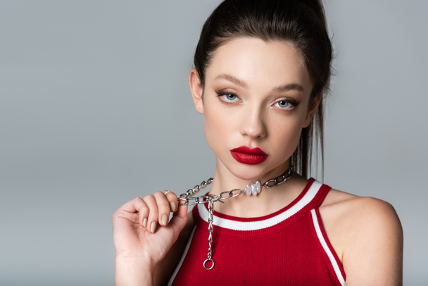 young stylish woman with red lips pulling necklace chain isolated on grey - Foto, afbeelding