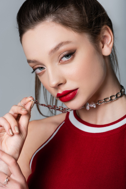 young model with red lips pulling necklace chain isolated on grey - Photo, Image